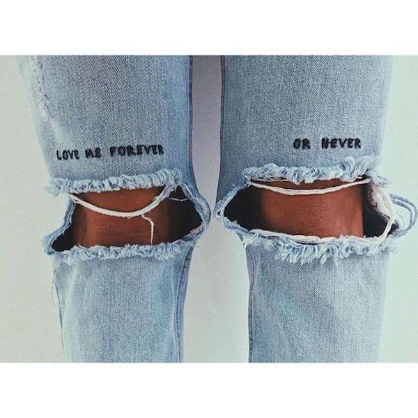 imagem mostra calça jeans com joelhos rasgados e as frase love me forever or never bordada à mão
