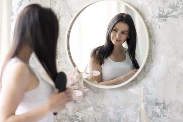 Imagem mostra mulher se olhando no espelho e pronta para fazer hidratação com clara de ovo