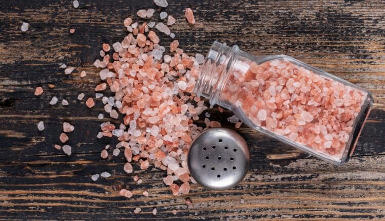 Himalayan salt coming out of open salt shaker on a dark wooden background. top view.
