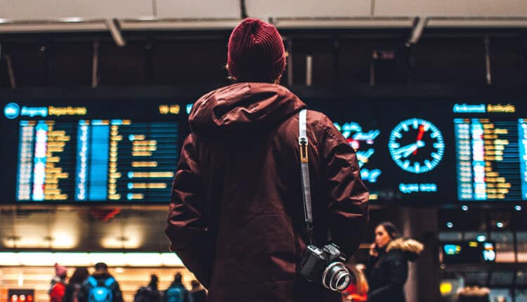 Homem diante de painel de aeroporto: qual a viagem perfeita para cada signo?