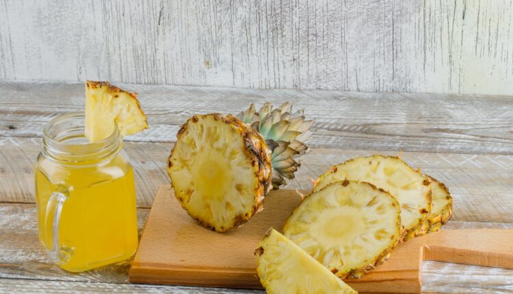 Pineapple with juice, cutting board high angle view on wooden and grungy background